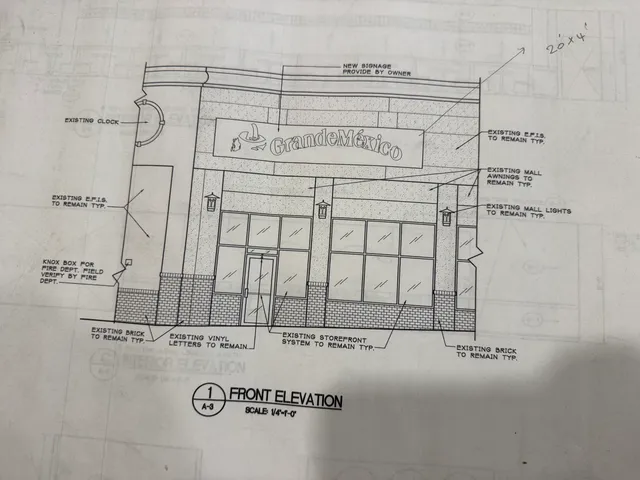 Front elevation drawing of an existing storefront façade showing the proposed 'Grande México' sign mounted above the entrance. The drawing also labels existing architectural elements to remain, including windows, brick base, awnings, lights, and a clock.
