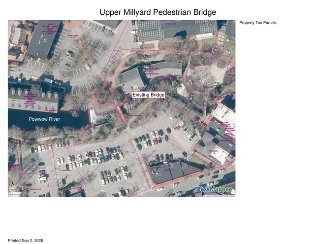 A parcel map overlaid on aerial imagery of the Upper Millyard area, showing the Powwow River, surrounding buildings, parking lots, and the labeled existing bridge location near the river crossing.