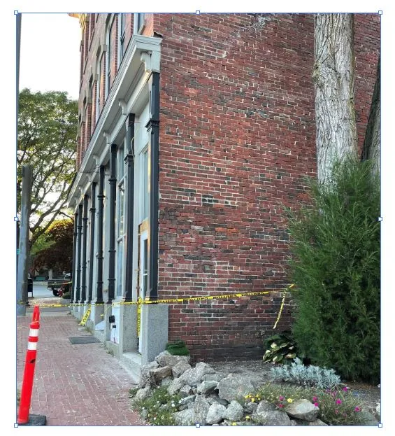 Existing street-level photo of the side of a brick building at 11 Elm St, showing the sidewalk, storefront facade, trees, and a taped-off area where the sign location appears to be.