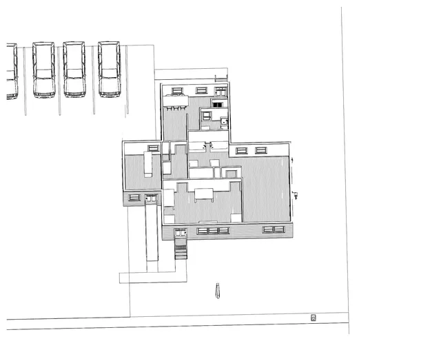 Black-and-white site plan showing the proposed building footprint, parking stalls, and access/driveway layout on the lot. The main structure is drawn in plan view with surrounding open yard and street frontage along the bottom edge.