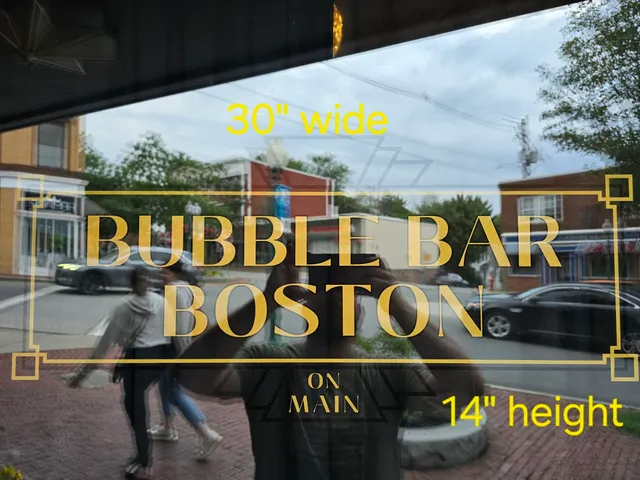 Photo of a storefront window showing a proposed gold "BUBBLE BAR BOSTON" sign layout with dimensions marked in yellow. The sign is pictured against the street reflection on Main Street, with the existing building and storefront visible behind it.